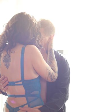 Two people embracing intimately with sun flare in background, one wearing blue lingerie and visible tattoos.