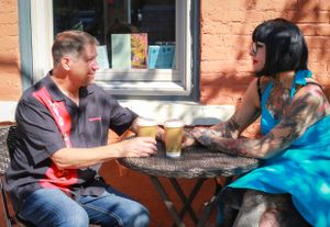 Two people enjoy coffee and conversation at an outdoor cafe table on a sunny afternoon.
