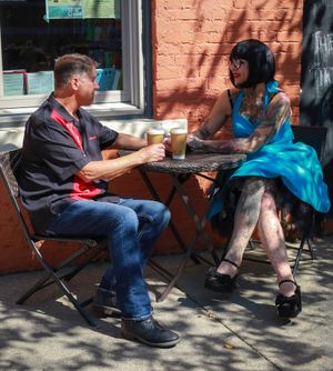 Two people enjoying coffee and conversation at a sidewalk cafe table on a sunny afternoon.