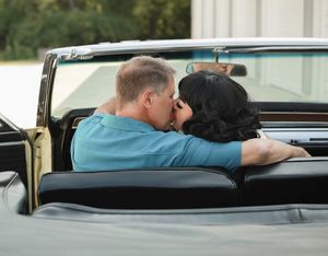 A couple shares a romantic moment while sitting in a classic vintage convertible car.