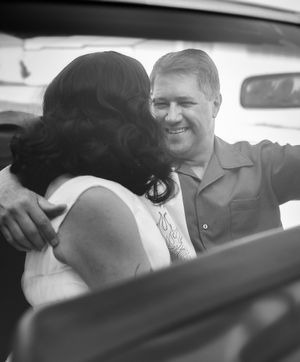 A black and white photograph showing an intimate moment between a couple sitting in a car.