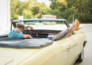 Someone relaxing with feet up in a cream-colored vintage convertible car on a sunny afternoon.