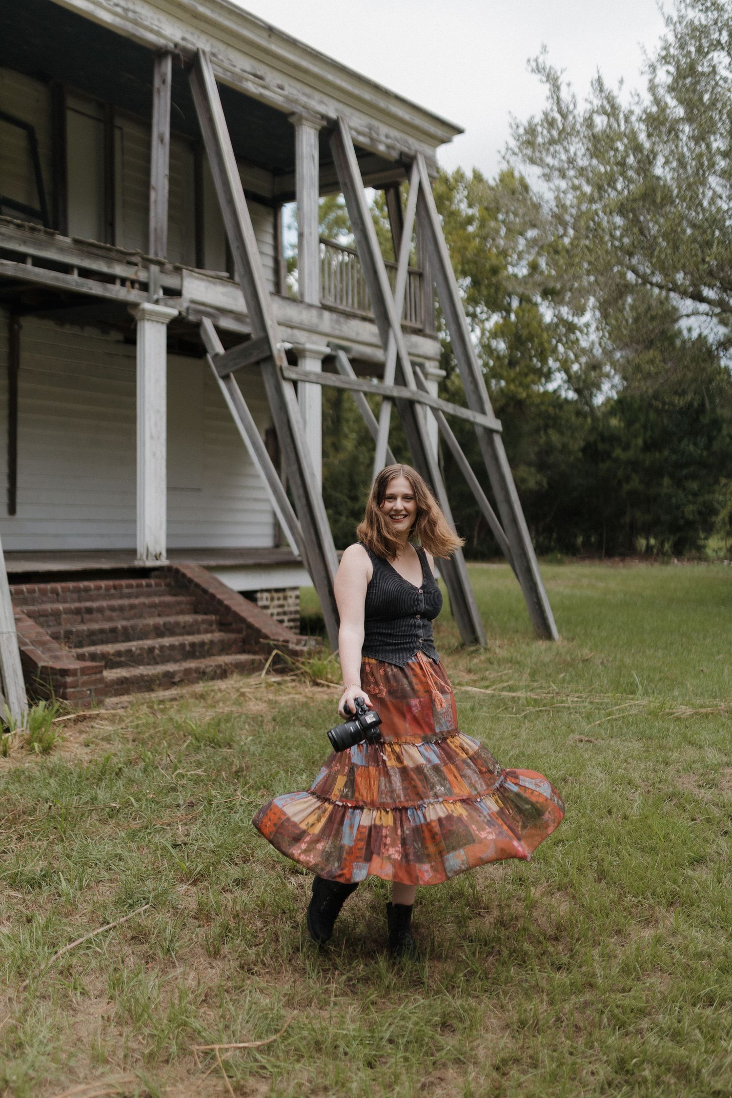 Smiling female photographer holding camera near large windows in brick building.