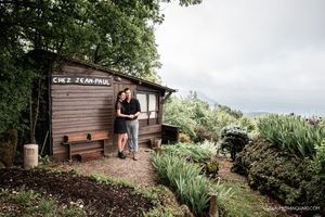 Rustic wooden cabin nestled among trees and landscaped gardens on a hillside.
