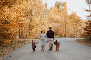 Famille marchant en forêt à l’automne avec leur chien, feuilles dorées en arrière-plan.