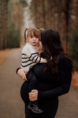 Maman enceinte tenant sa fille dans un sentier forestier, moment intime capturé en automne.