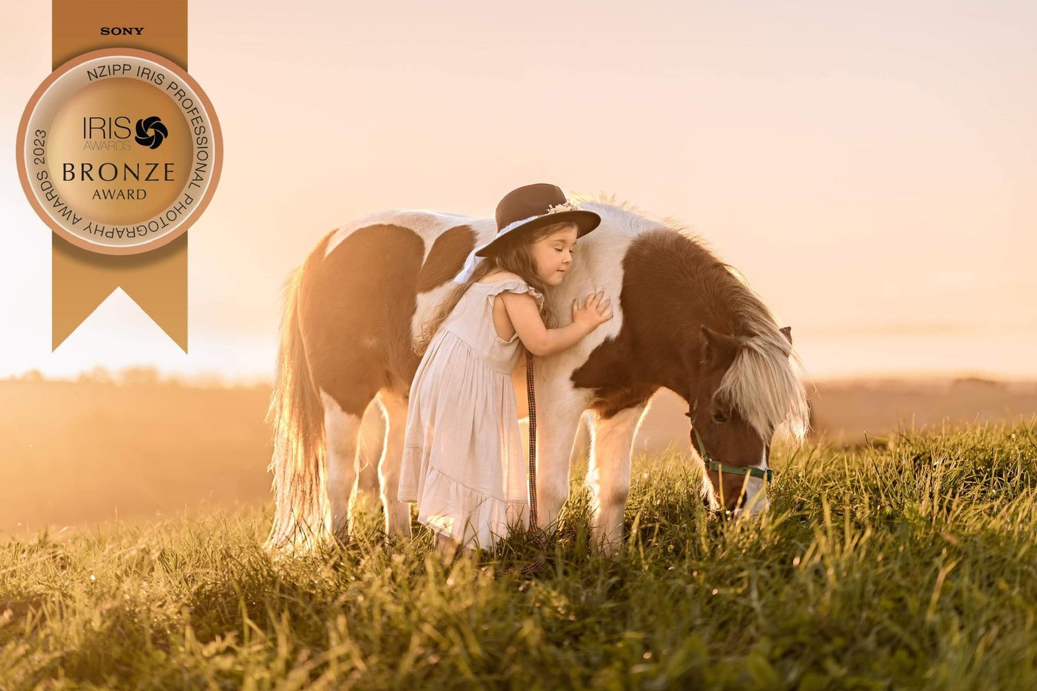 A peaceful scene with horses and a figure in a flowing dress at golden hour.