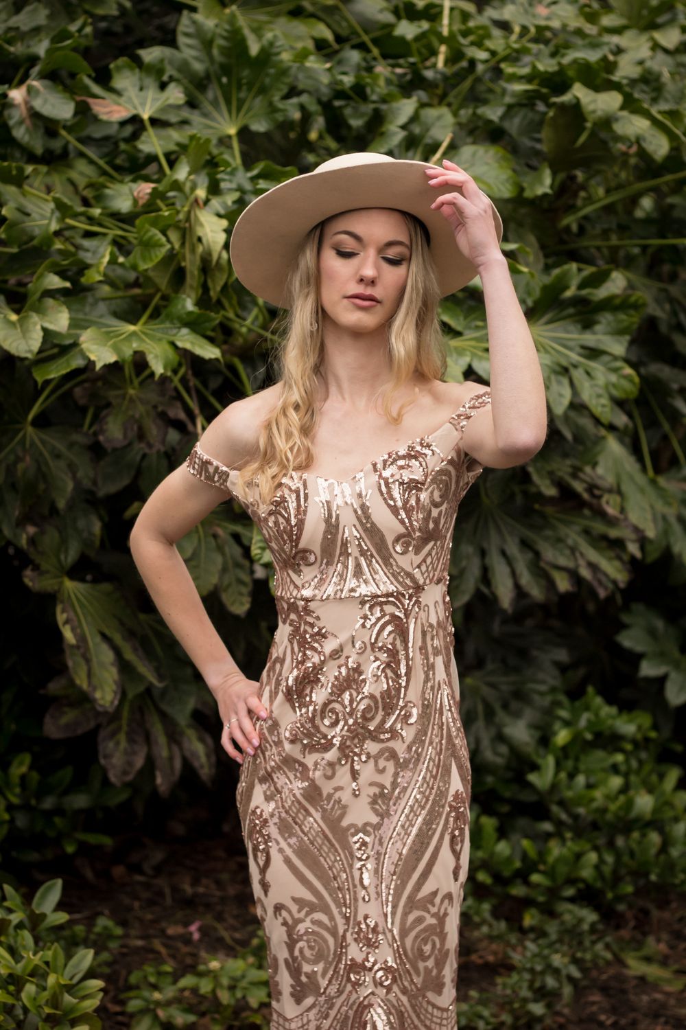 Vintage-inspired portrait in detailed beaded dress and neutral hat against garden setting.