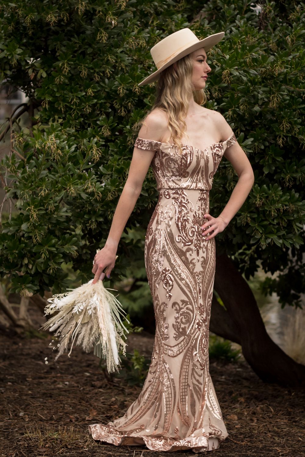 A formal dress photoshoot featuring a sequined gown, wide-brim hat, and dried pampas grass bouquet.