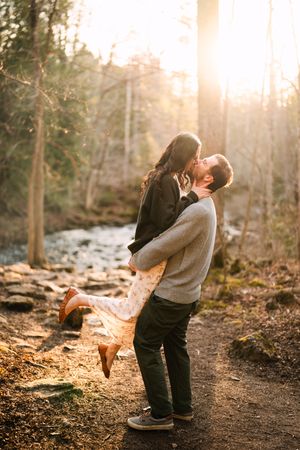 Couple sharing an intimate moment on a forest trail during golden hour.
