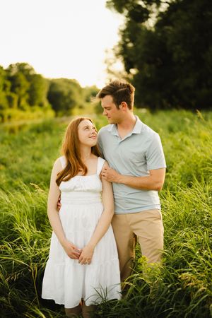 A romantic couple poses in tall grass during golden hour.