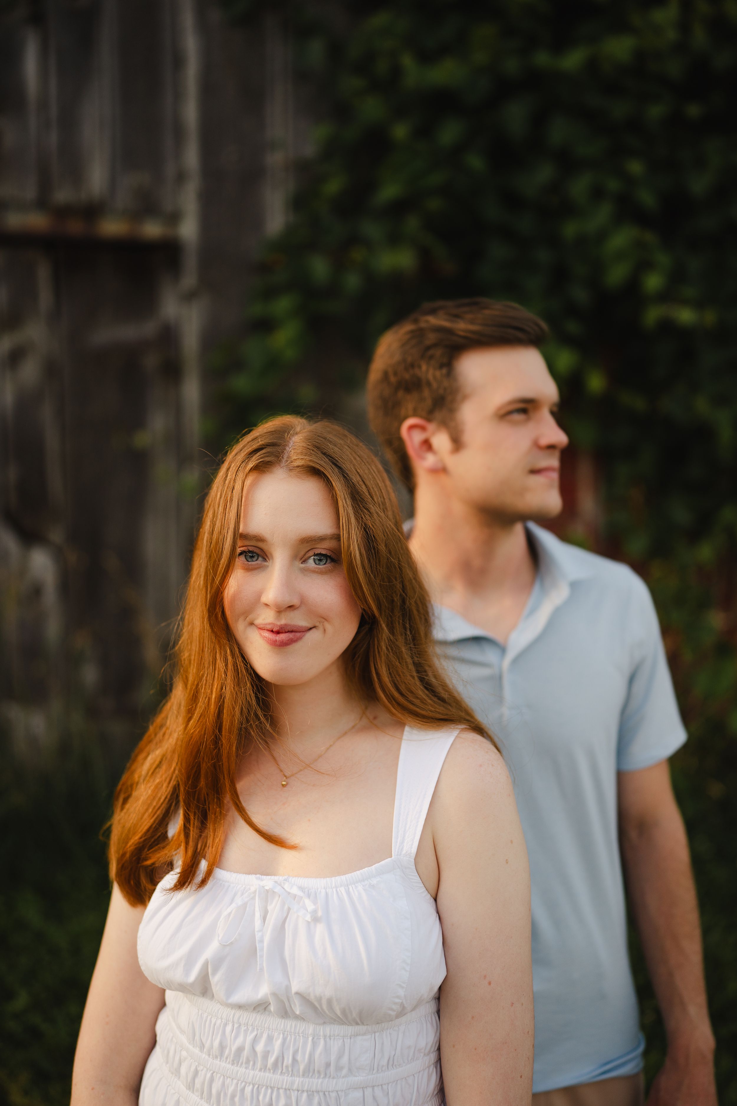 A couple in casual summer attire posing against a rustic wall.