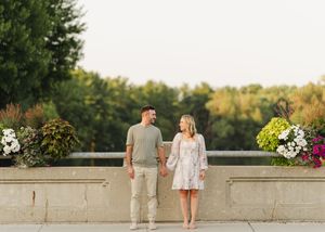 Couple standing together on a stone wall during golden hour at sunset.