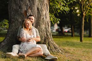 Romantic couple sitting together under a large tree in a park setting.