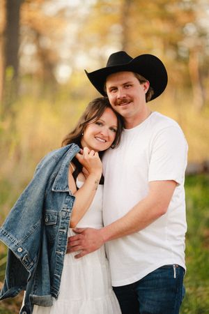 Couple in casual western attire embracing in autumn field at sunset.
