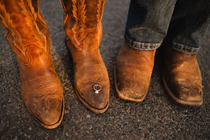 Row of worn brown cowboy boots lined up on dark pavement.