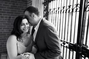 Black and white portrait of couple sharing romantic moment by ornate iron gate.