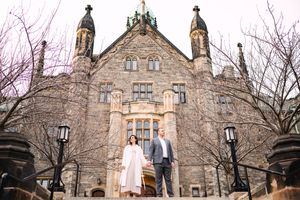 Wide angle shot of couple standing in front of gothic stone church architecture.