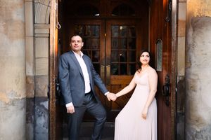 Romantic couple poses together in front of historic stone building during engagement photoshoot.