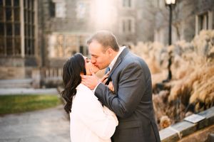 Couple shares intimate moment against stone architecture during sunset engagement session.