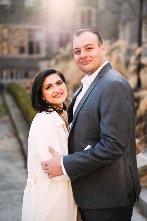 Couple embraces while wearing formal attire against stone building backdrop.