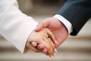 Close-up of couple holding hands showing engagement ring detail.