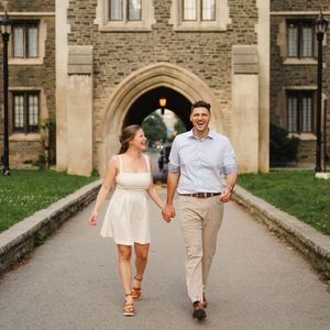 Couple walking hand in hand along stone path by historic building.