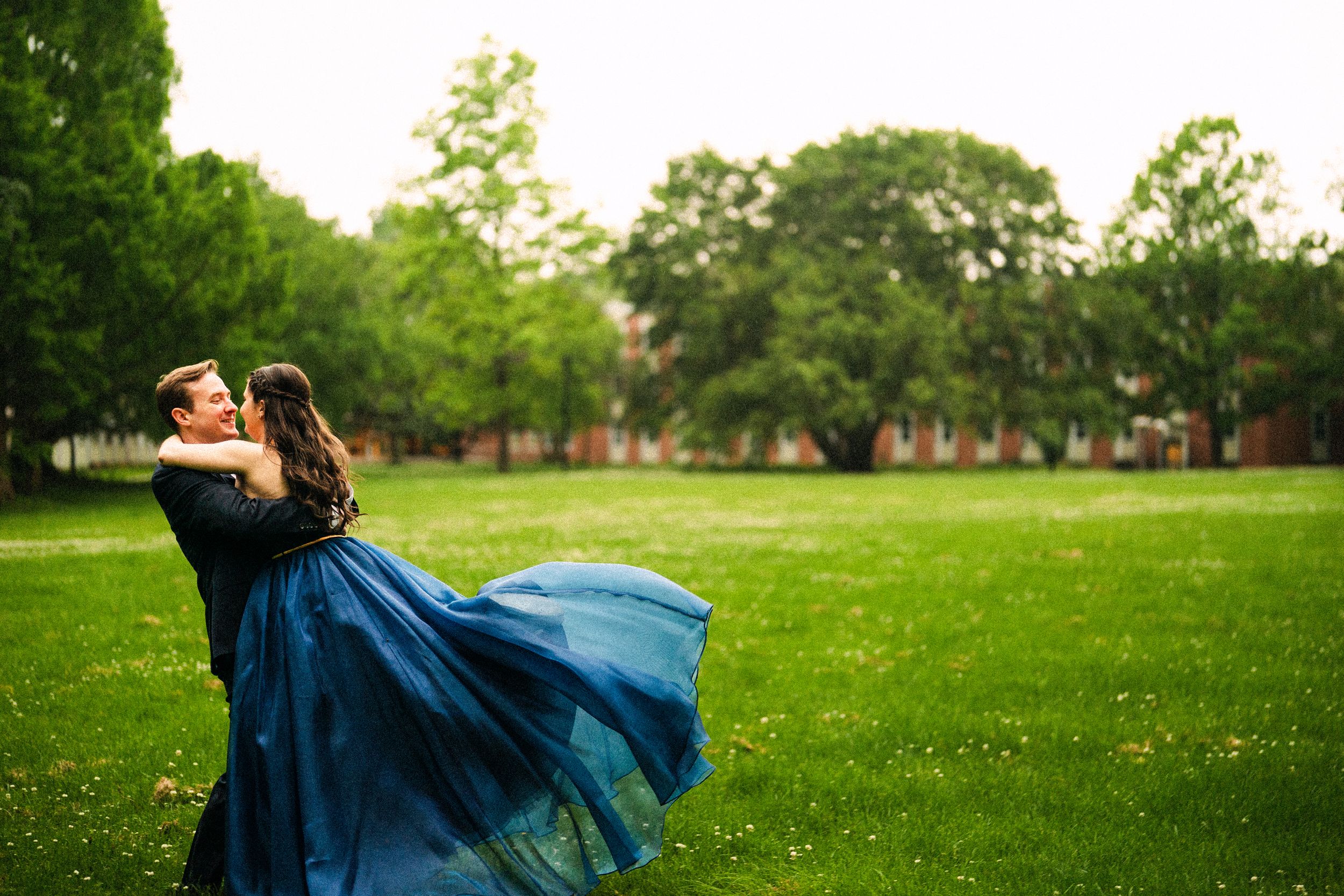 Couple dancing playfully in a green park during golden hour with flowing blue dress movement.