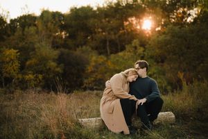 Couple sits together on hill during golden hour engagement session.