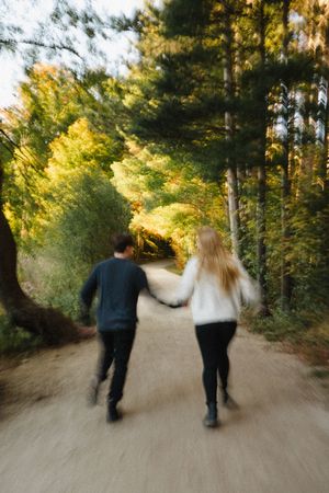 Two people walking together on a wooded path in motion blur during golden hour.