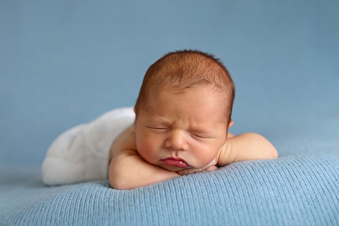 Peaceful sleeping newborn baby resting on soft blue blanket in natural light.