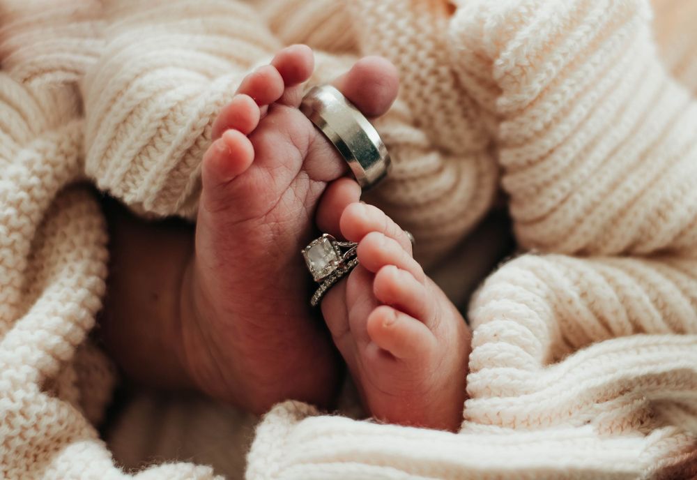 Close-up of newborn baby feet wrapped in knit blanket adorned with wedding rings.