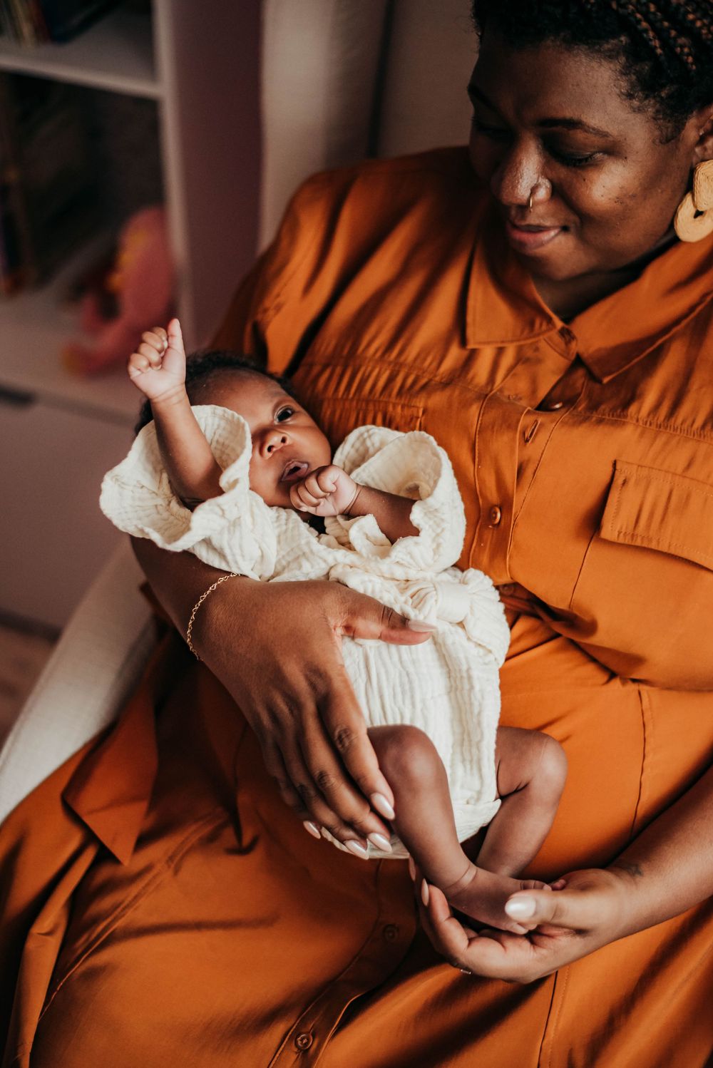 Smiling mother in orange dress cradling active newborn baby during in-home lifestyle photo session.