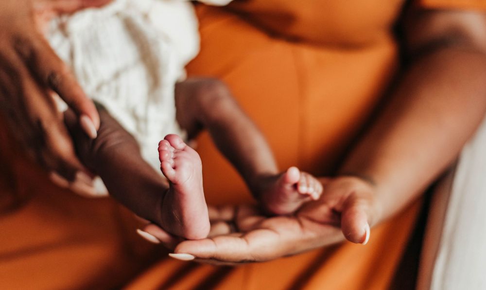 Close-up of newborn baby tiny feet cradled gently in mother's hands against orange background.