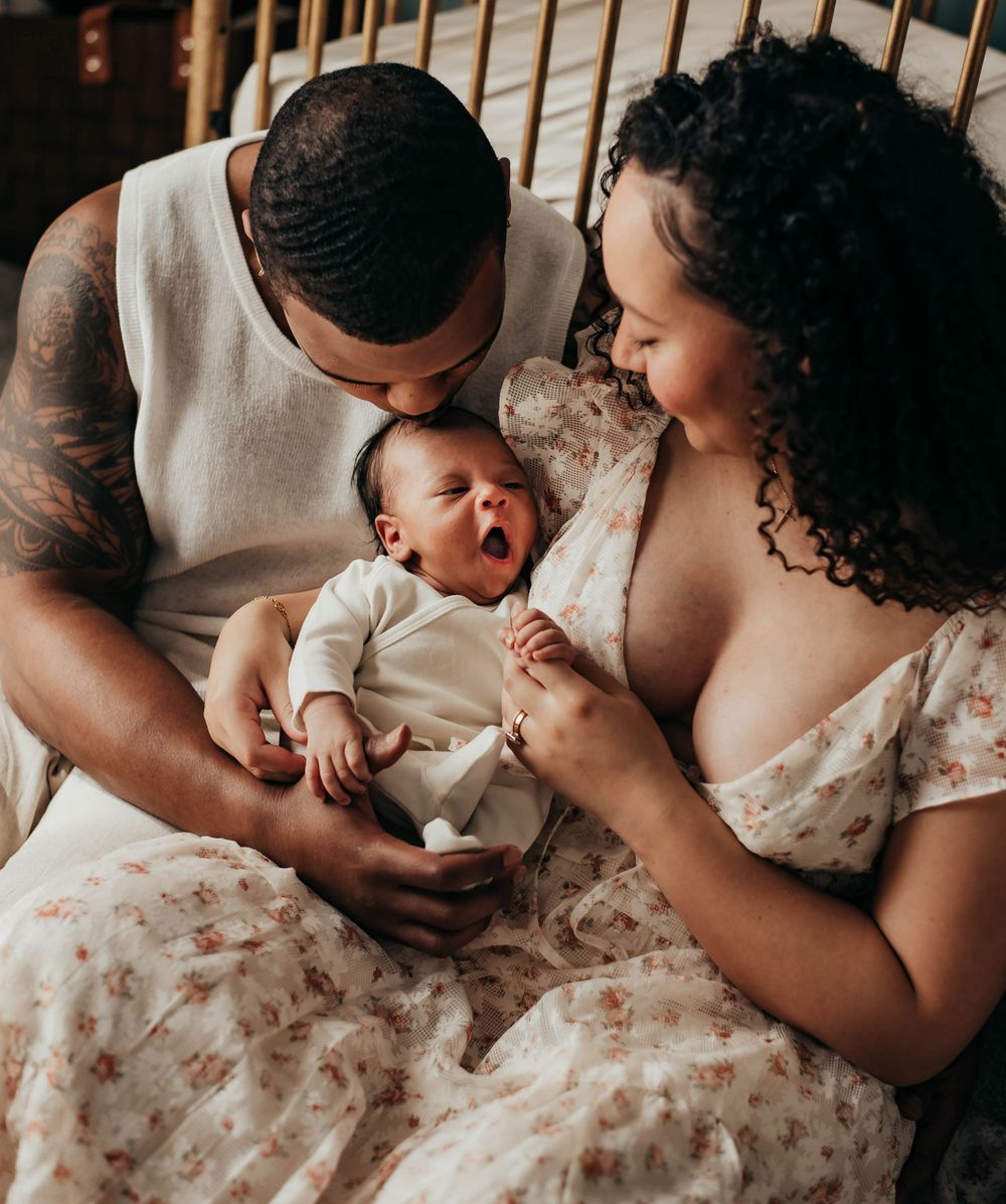 New parents lovingly watching yawning newborn baby during intimate indoor newborn photo session.