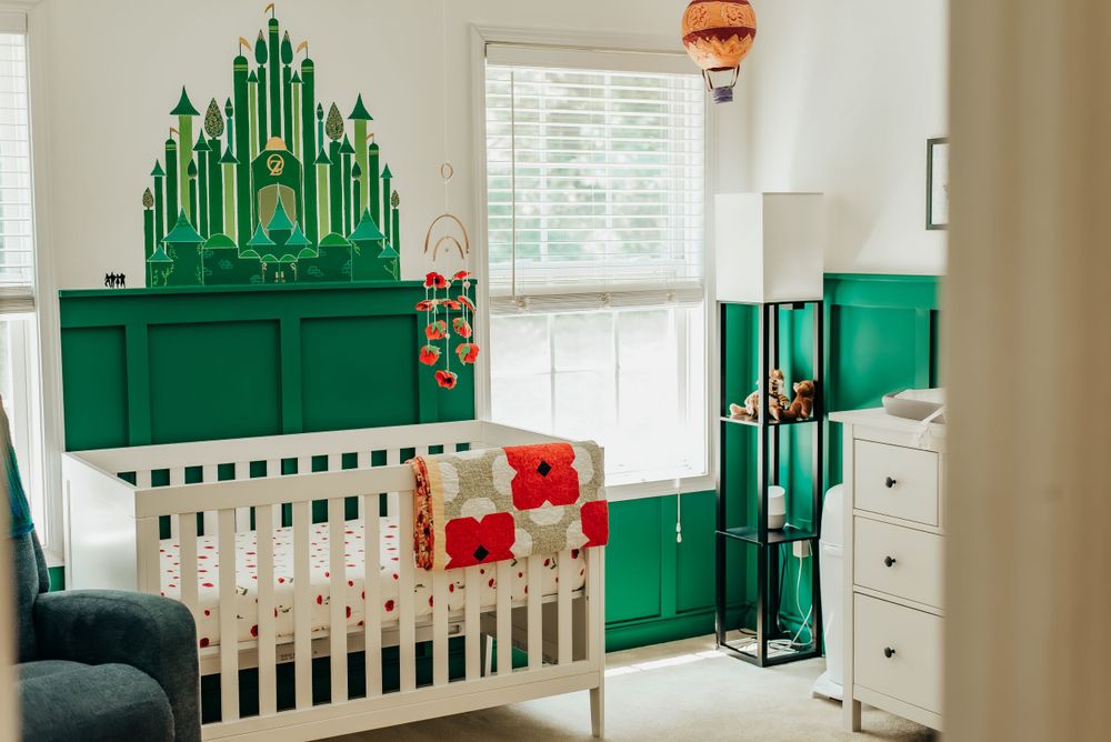 Wizard of Oz themed nursery with emerald city mural, green wainscoting, and white crib.