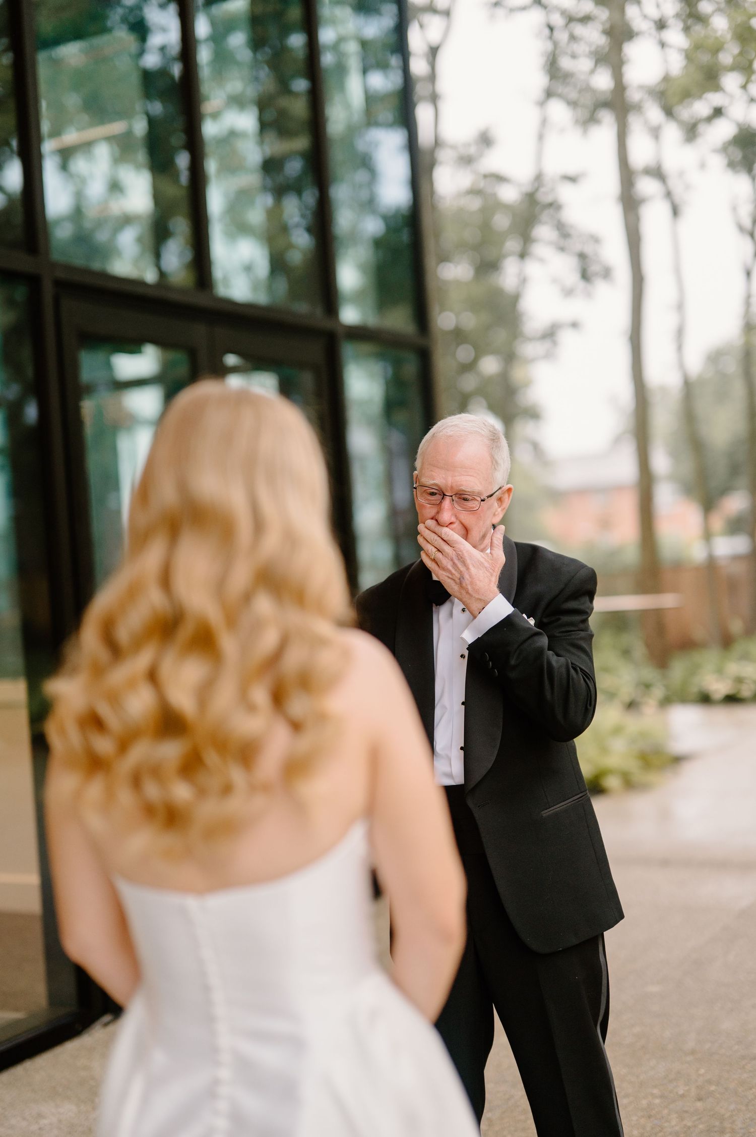 Emotional father seeing bride daughter in wedding dress for the first time, covering mouth in surprise.