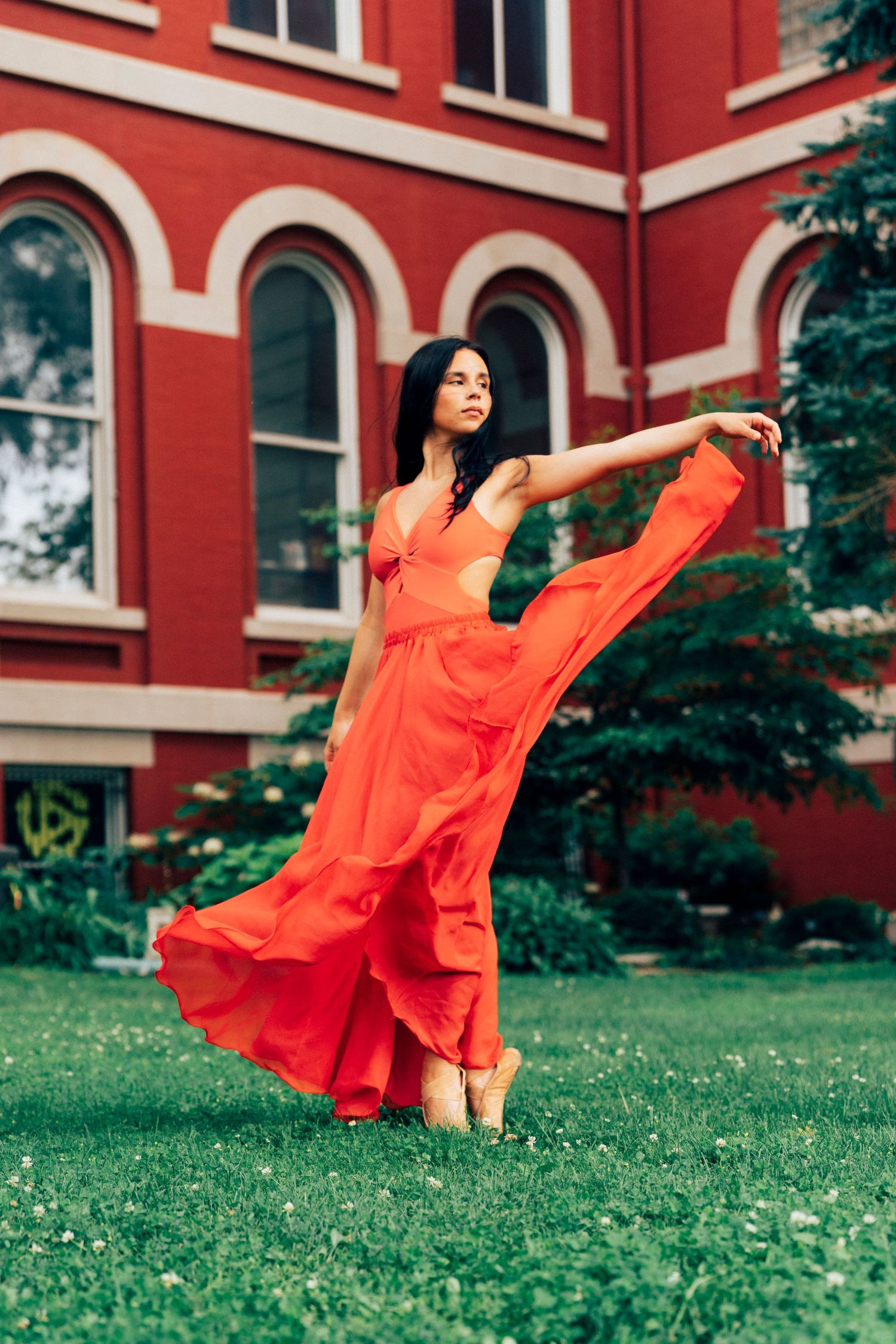Senior portrait photographer captures professional dancer in red dress reaching out on the courthouse lawn, Crown Point.