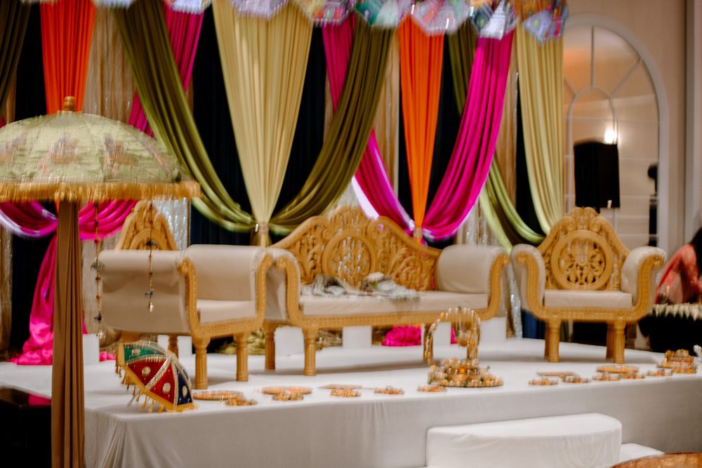 Colorful Indian wedding mandap with gold ornate chairs, vibrant pink, green, and orange draping decorations.