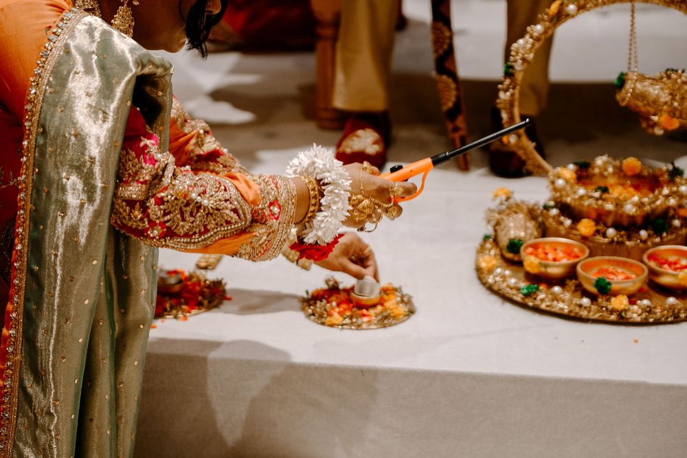 Close-up of ornate Hindu wedding ceremony rituals with decorated hands, diyas, and traditional gold jewelry on white altar.