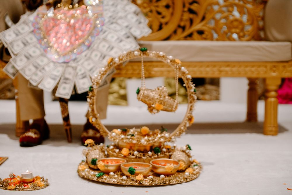 Traditional Indian wedding decorative tray with gold ornaments, miniature swing, and diyas on white floor.