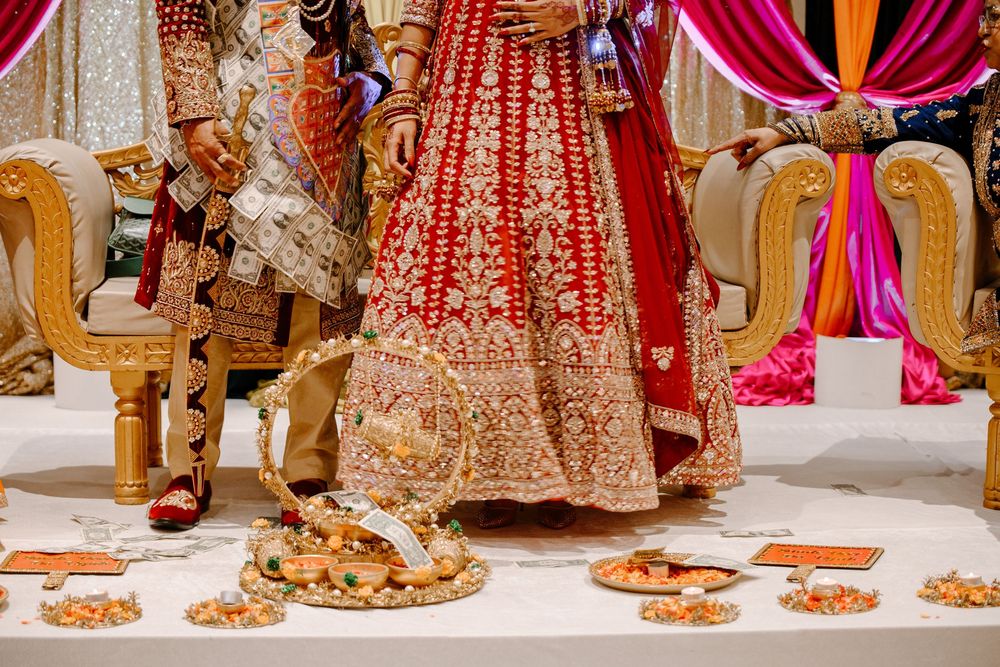 Indian bride in red and gold embroidered lehenga stands at traditional Hindu wedding ceremony with ritual offerings on floor.