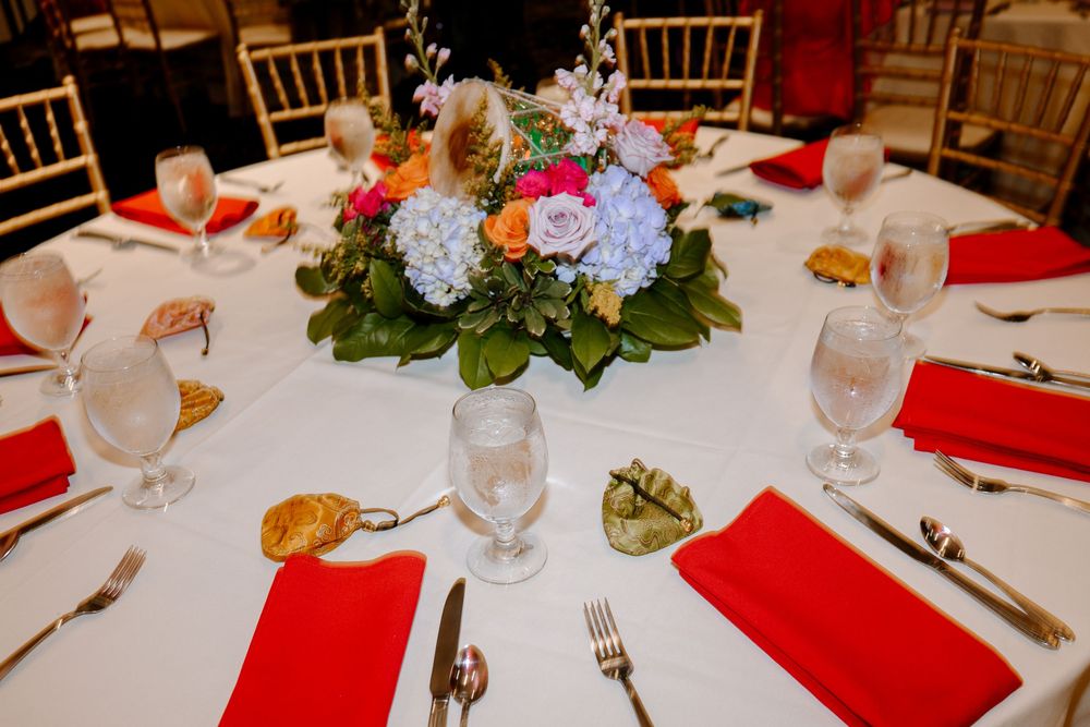 Elegant round wedding reception table with red napkins, crystal glasses, and a colorful floral centerpiece of hydrangeas and roses.