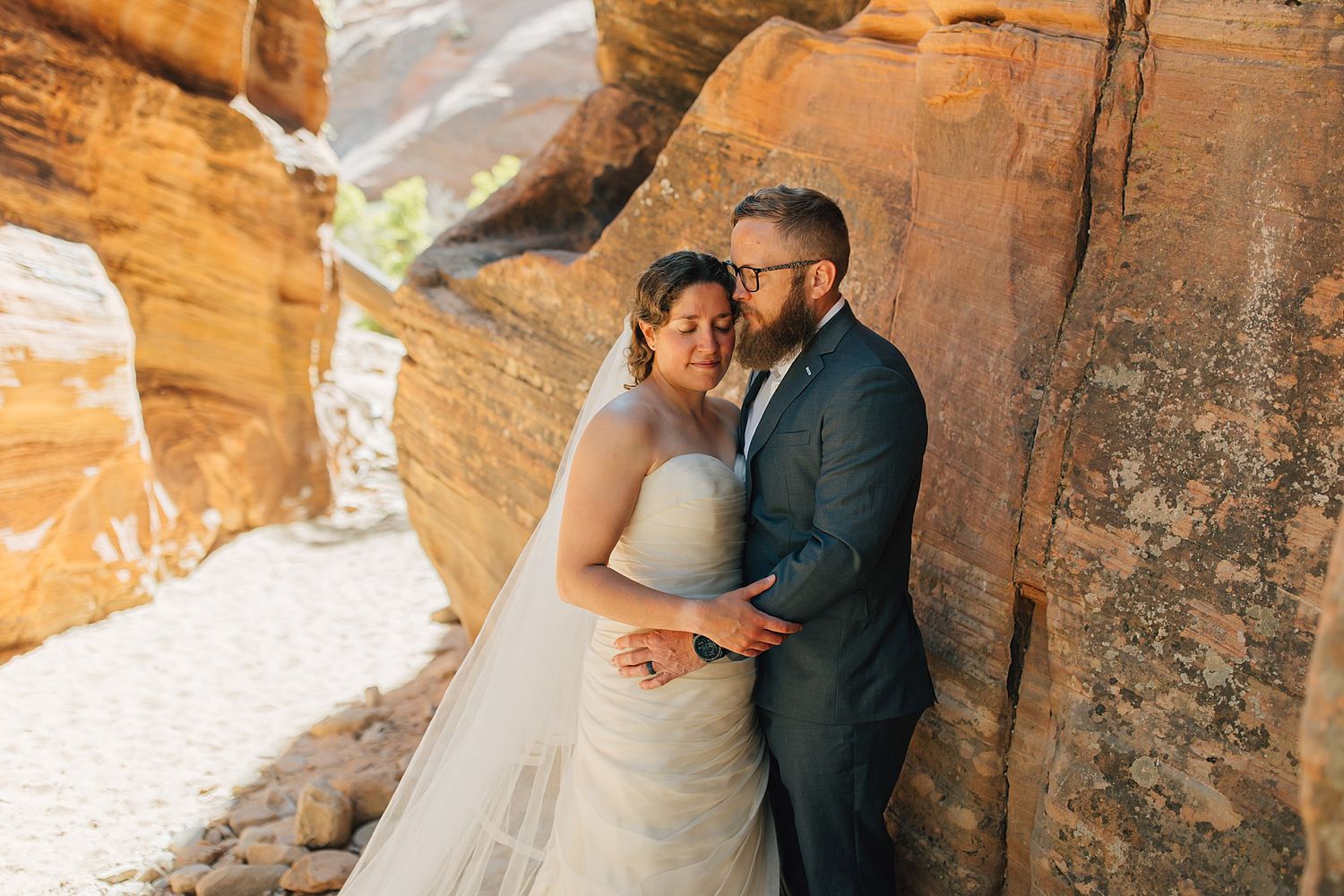 A bride and groom share a romantic moment leaning against red rock canyon walls during their outdoor desert wedding.