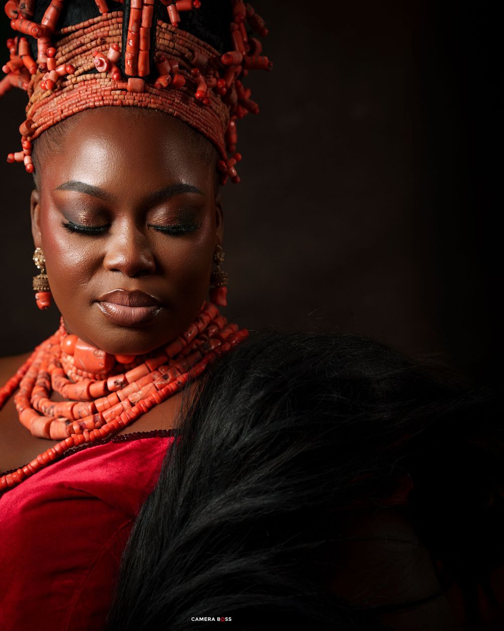 Woman in traditional Nigerian coral beaded crown and necklace wearing red velvet dress with black fur accessory.
