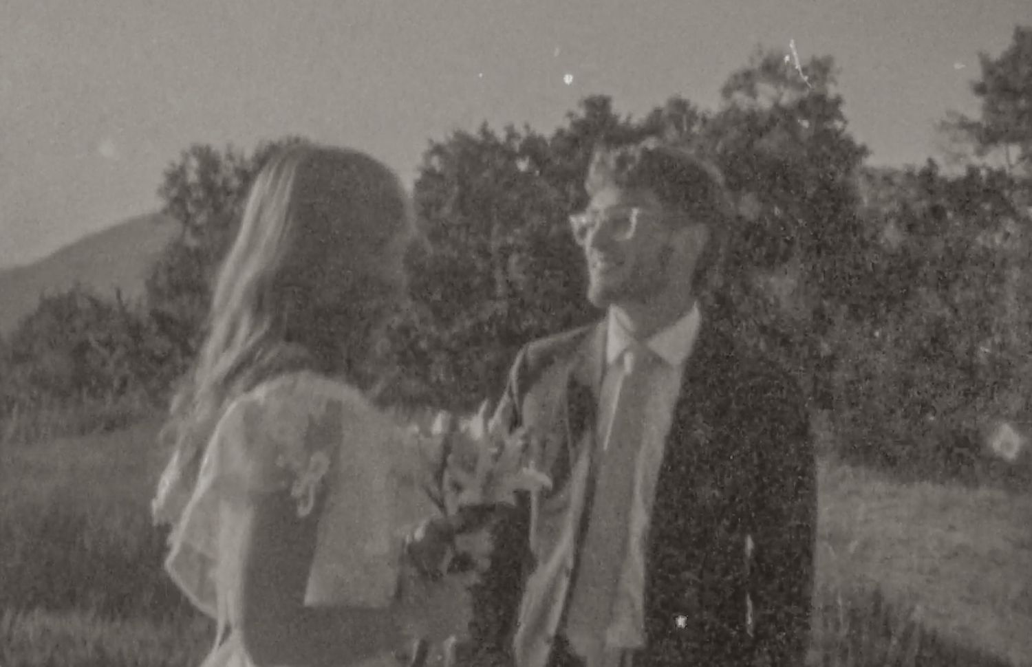 Black and white photo of a couple sharing a romantic moment outdoors at a wedding ceremony.