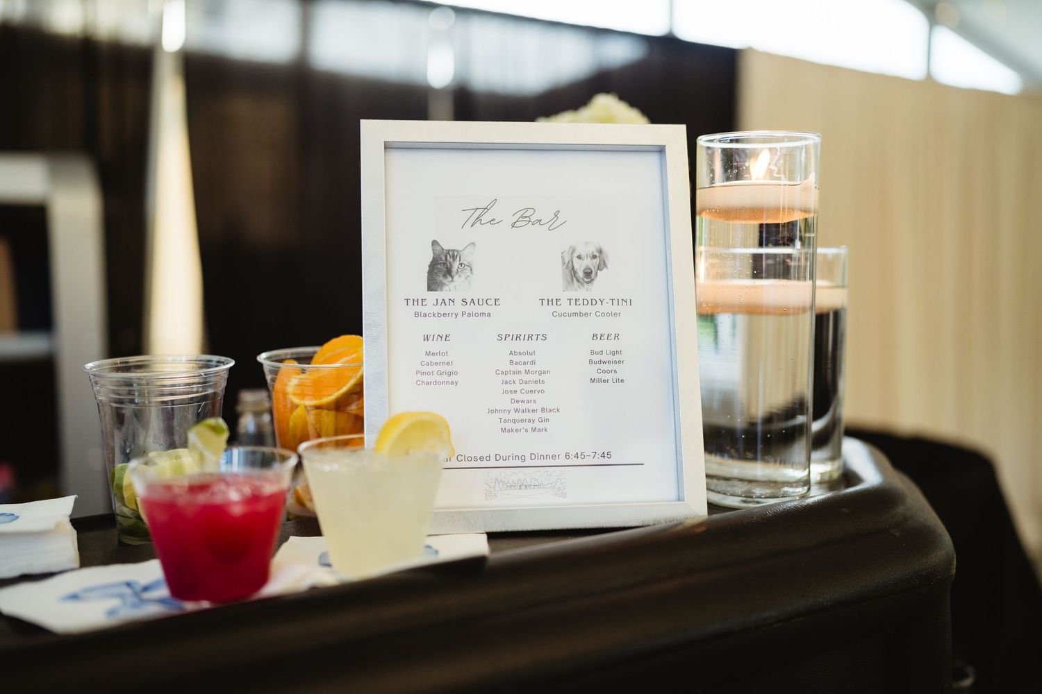Elegant wedding cocktail bar display with signature drink menu, colorful cocktails, and candle centerpiece.