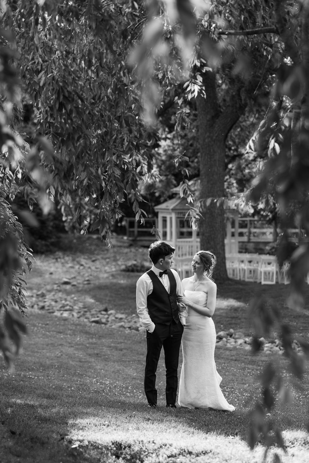 Black and white photo of a bride and groom standing under a willow tree in a garden setting at the civic garden complex in london, ontario.