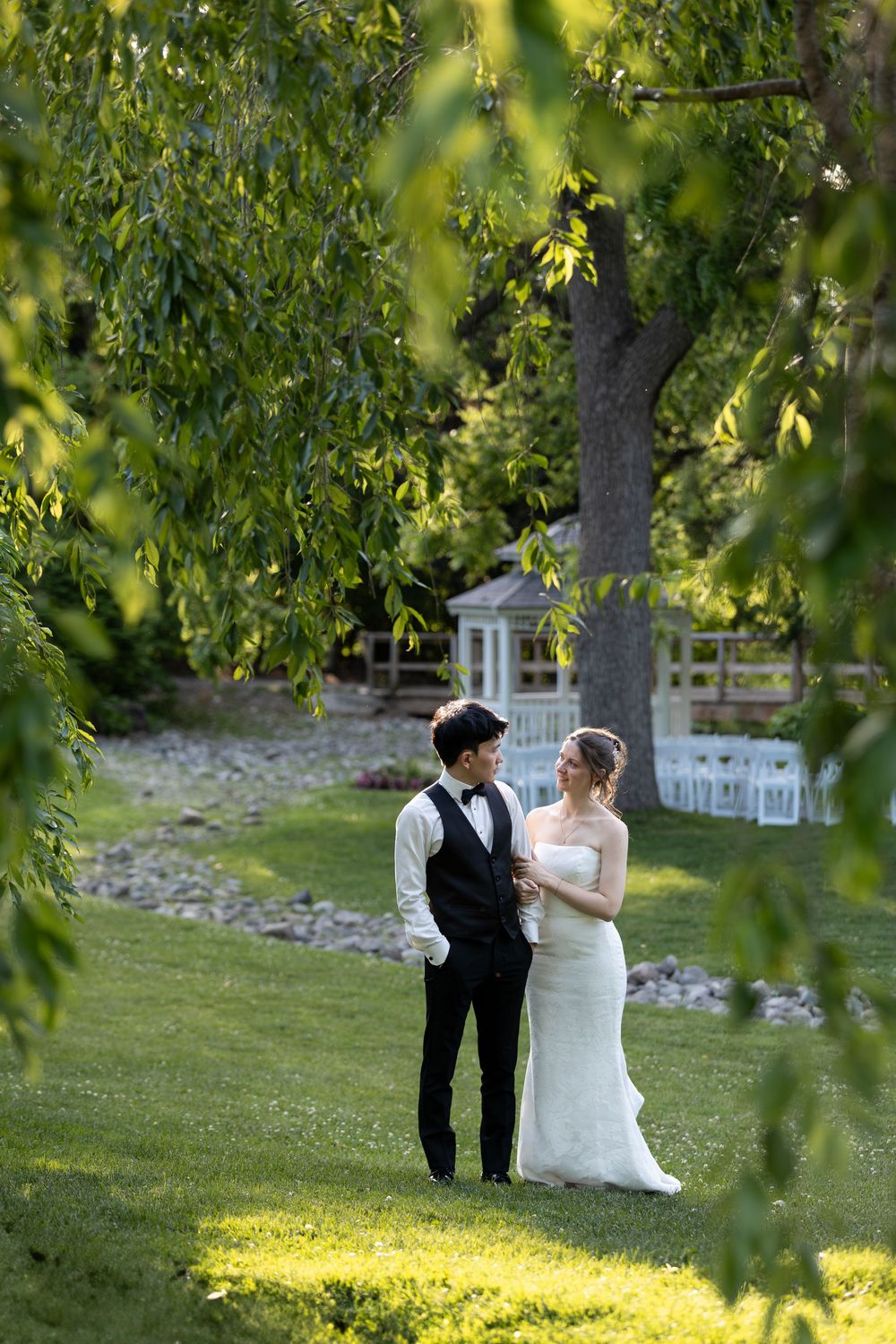 Bride and groom share a romantic moment on lush green lawn framed by willow tree branches at the civic garden complex in london, ontario.