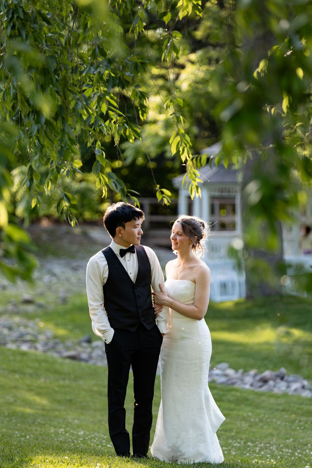 Bride and groom share a romantic moment under lush green trees on a sunny wedding day at the civic garden complex in london, ontario.